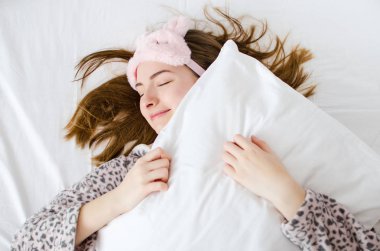 Happy young woman enjoying sunny morning hugging pillow. Rest, sleeping, comfort concept - caucasian girl lying in the bed at home bedroom and smiling after wake up. View from above. clipart