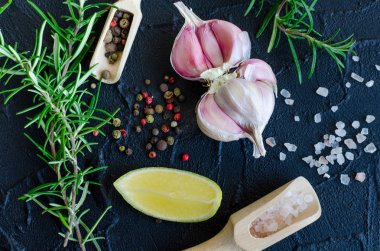 Otlar ve baharatlar seçimi - biberiye, sarımsak, limon, tuz ve karabiber karanlık taş masada. Pişirme malzemeleri kavramı. Gıda düz yatıyordu. Üstten Görünüm.