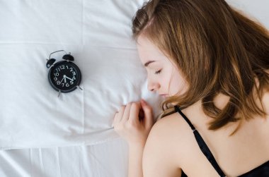 Genç kadın çalar saat sabah yastıkta yatmak. Uyuyan kız ve alarmclock evde yatak odasında. Öğrenci ya da öğrenci geç uyanmak korkuyor. Çalar saat anksiyete. Kavram fazla uyumak.