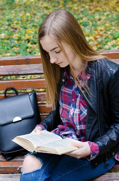 Beautiful teen girl reading a book. Teenage or young adult high school or college student studying in the park.