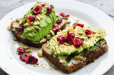 Kahvaltıda sağlıklı avokado tostları ya da öğle yemeğinde çavdar ekmeği, krem peynir, roka, dilimlenmiş avokado, kızılcık, balkabağı, kenevir ve susam tohumu. Vejetaryen sandviçler. Temiz yeme kavramı.