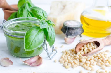 Pesto Cenova - geleneksel İtalyan yeşil fesleğen sos ile beyaz ahşap zemin üzerinde ham maddeler. Harç, Parmesan peyniri, çam fıstığı, zeytin yağı, sarımsak ve tuz fesleğen yaprağı.