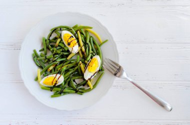 Taze yaz sıcak haşlanmış yumurta ve sos Balzamico glassa ahşap arka plan üzerinde beyaz plaka ile pişmiş yeşil fasulye salatası. Sağlıklı beslenme. Vejetaryen yiyecekler kavramı. Üstten görünüm. Kopya alanı.