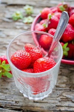 Bir kaşık ile cam çilek yemeye hazır. Sulu sulu taze Olgun kırmızı çilek bir eski ahşap dokulu masa üstüne. Sağlıklı snack.