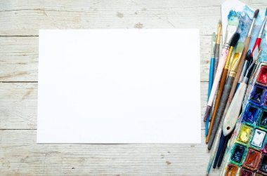 Sanatçı boya fırçaları ve ahşap zemin üzerinde suluboya boya boya kutuları ve boş kağıt yaprakları. Yaratıcı eğlence için aletler ve aletler. Resim sanatı konsepti modeli. Üst Manzara. Uzayı kopyala Düz yatıyordu.