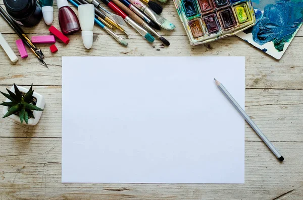 Yaratıcı sanatçı işyeri düz yatış, maket. Masanın üstünde boş kağıtlar, boya fırçaları ve boya paletleri var. Sanat, atölye, resim, çizim, zanaat, yaratıcılık konsepti. Boşluğu kopyala.