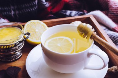 Bal, zencefil kökü ve sonbahar düşen yapraklar üzerinde kırmızı sıcak yün battaniye ile ahşap tepsi üzerinde limon ile sağlıklı zencefil çayı. Sıcak içecek soğuk yağmurlu günler için. Grip karşı doğal tıp.