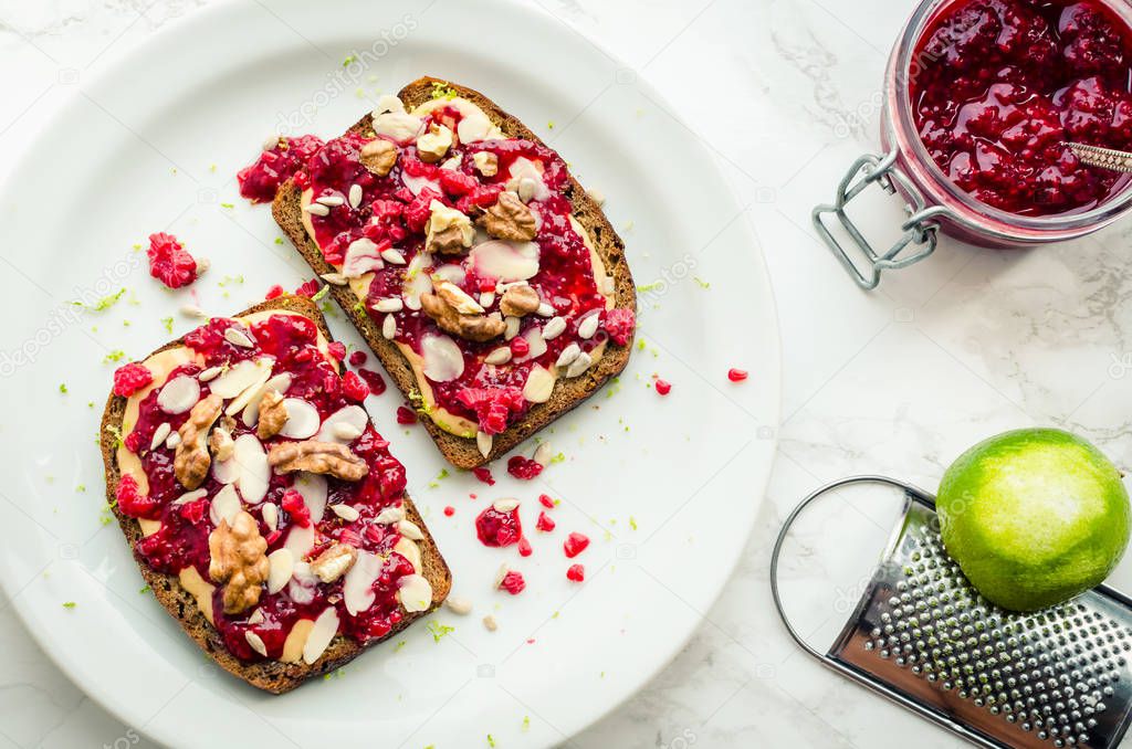 Toasts with peanut butter, homemade raspberry chia jam, walnuts, almonds and sunflower seeds on white marble background. Healthy idea for breakfast toasts. Superfoods and healthy food concept. Top view.