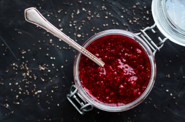 Chia tohum içinde siyah arka plan üzerine kaşıkla bir kavanoza ile ev yapımı çilek reçeli. Kahvaltı tost için sağlıklı bir fikir. Superfoods ve sağlıklı gıda kavramı. Üstten görünüm.
