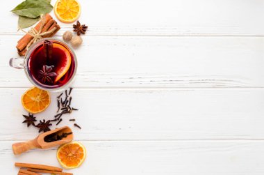 Sıcak kırmızı mulled şarap veya cam portakal, tarçın ve anasonu baharat ve malzemelerin üzerine beyaz tahta arka plan ile ile gluhwein. Baharatlı sıcak içecek. Mevsimlik sıcak içecek. Kopya alanı.