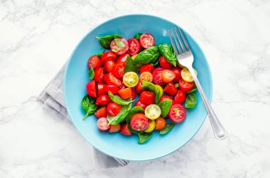 Taze parlak domates salatası fesleğen, zeytinyağı ve balsamik sirke beyaz mermer arka plan ile kiraz kırmızı ve sarı domates. Vejetaryen ve vegan gıda. Kavramı bir lezzetli ve sağlıklı yemek için. Üstten görünüm. Kopya alanı.