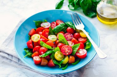 Taze parlak domates salatası fesleğen, zeytinyağı ve balsamik sirke beyaz mermer arka plan ile kiraz kırmızı ve sarı domates. Vejetaryen ve vegan gıda. Kavramı bir lezzetli ve sağlıklı yemek için.