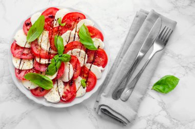Tabak sağlıklı klasik lezzetli caprese salatası ile olgun domates ve mozzarella peyniri taze fesleğen ile beyaz mermer zemin üzerine bırakır. İtalyan mutfağı kavramı. Üstten görünüm.