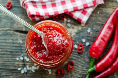Kırmızı sıcak biber reçeli cam eski ahşap zemin üzerine taze malzemelerle. Doğal ev yapımı biber sosu kaşıkla. Taze ev yapımı salsa sosu. Üstten görünüm.