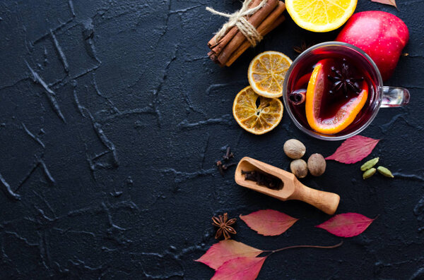 Autumn mulled wine based on red wine with orange, apple and spices cinnamon sticks, star anise, nutmeg, cardamom and clove on black background. Seasonal beverages recipe. Top view. Copy space.