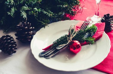 Aile Noel kutlaması sofra konsepti. Köknar ağacı dalları, mumlar ve çam kozalaklarının doğal süslemeleriyle bayram yemeği için güzel bir yer..