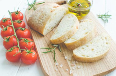 Biberiye, tuz, domates ve zeytinyağı ile beyaz rustik tabloda ahşap kesme tahtası üzerinde taze pişmiş ciabatta ekmeği dilimlenmiş. İtalyan gıda kavramı.