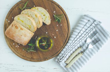 Ciabatta ekmeği zeytin yağı ve biberiye ile ahşap tahta üzerinde beyaz ahşap masa üzerinde dilimlenmiş. İtalyan gıda kavramı. Üstten görünüm.
