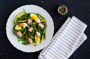 Pişmiş fasulye, ton balığı, haşlanmış yumurta ve sos Balzamico glassa siyah taş zemin üzerine beyaz tabak içinde taze yaz sıcak salatası. Sağlıklı beslenme kavramı. Üstten Görünüm.