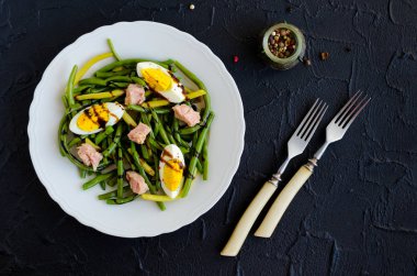 Pişmiş fasulye, ton balığı, haşlanmış yumurta ve sos Balzamico glassa siyah taş zemin üzerine beyaz tabak içinde taze yaz sıcak salatası. Sağlıklı beslenme kavramı. Üstten Görünüm.