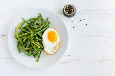 Metin için yer ahşap zemin üzerine beyaz tabak içinde kızarmış yumurta ile yeşil fasulye pişirdim. Sağlıklı vejetaryen gıda kavramı. Üstten Görünüm. Kopya alanı.