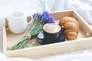 Romantik yaz odaya yatak, taze kruvasan ile tepsi, fincan sütlü kahve espresso ve mavi Peygamber buket. Günaydın kavramı. Yavaş hayattan zevk. Geleneksel kahvaltı.