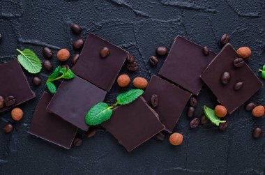 Kahve çekirdekleri şeker ile koyu çikolata, çikolata ile kaplı ve siyah arka plan üzerine yeşil nane yaprakları. Üstten görünüm.