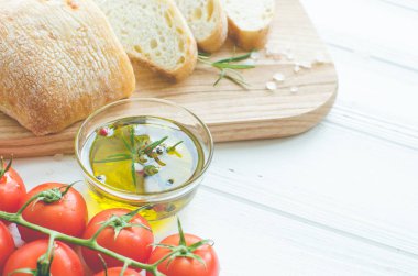 Biberiye, tuz, zeytin, domates ve zeytinyağı ile beyaz rustik tabloda ahşap kesme tahtası üzerinde taze pişmiş ciabatta ekmeği dilimlenmiş. İtalyan gıda kavramı. Kopya alanı.