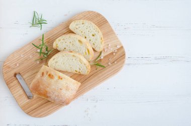 Biberiye ve tuz ile beyaz rustik tabloda ahşap kesme tahtası üzerinde taze pişmiş ciabatta ekmeği dilimlenmiş. Üstten görünüm. Kopya alanı.
