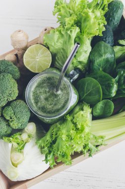 Yeşil sebze suyu malzemelerle bir mason kavanoza: ıspanak, kereviz, salatalık, marul, zencefil, limon ve brokoli Beyaz ahşap zemin üzerinde bir tepsi. Bahar Detoks kavramı. Üstten Görünüm. Kopya alanı.