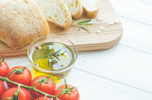 Biberiye, tuz, zeytin, domates ve zeytinyağı ile beyaz rustik tabloda ahşap kesme tahtası üzerinde taze pişmiş ciabatta ekmeği dilimlenmiş. İtalyan gıda kavramı. Kopya alanı.