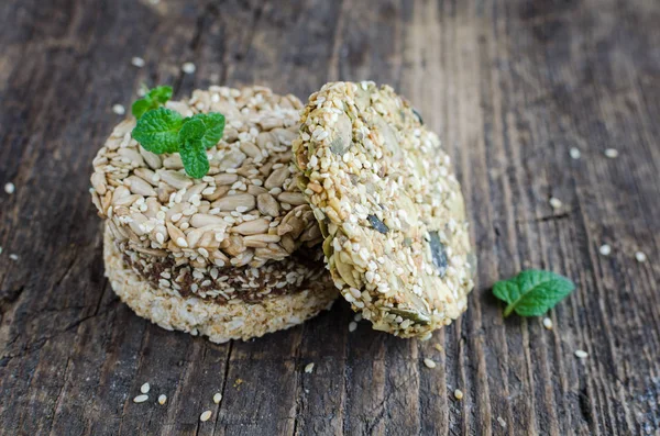 Dessert cereal snacks. Fitness dietary food. Kozinaki with sesame, peanuts, sunflower and pumpkin seeds and chocolate chip on old rustic wooden board, mint leaf. Vegetarian healthy nutrition concept.