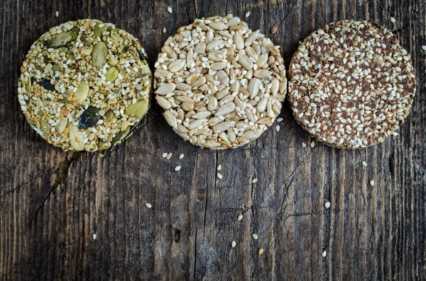 Dessert cereal snacks. Fitness dietary food. Three different kozinaki with sesame, peanuts, sunflower and pumpkin seeds, date on old rustic wooden board. Vegetarian concept. Top view. Copy space.