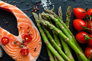 İki taze çiğ somon biftek sebze ve baharatlar ile: kuşkonmaz, domates, biber Mısır, tuz, biber biber, limon ve zeytin yağı siyah arka plan üzerine. Sağlıklı gıda diyet kavramı. Üstten görünüm.