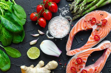 İki taze Çiğ somon biftek sebze ve baharatlar ile: kuşkonmaz, ıspanak, sarımsak, domates, zencefil, biber, tuz, biber, soğan ve siyah arka plan üzerine limon. Sağlıklı gıda diyet kavramı. Üstten Görünüm.