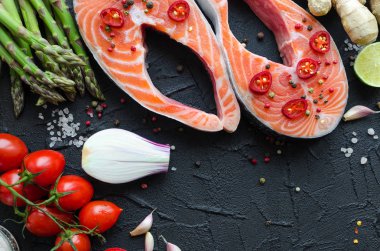 İki frash çiğ somon biftek ile kuşkonmaz, ıspanak, sarımsak, domates, zencefil, biber Mısır, tuz, biber, soğan ve siyah arka plan üzerine limon. Sağlıklı gıda diyet kavramı. Üstten görünüm. Yakın çekim. Kopya alanı