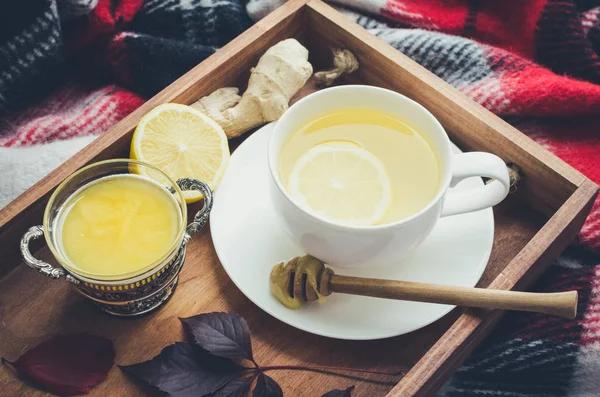 Hot healthy green tea with ginger and lemon on wooden tray with autumn fallen leaves on red warm woolen blanket. Relaxing in cold weather. Natural medicine against flu. Seasonal beverages.