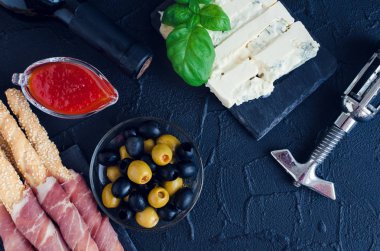 Bir şişe şarapla antipasti karanlık taş zemin üzerine. Grisini breadsticks prosciutto jambonu, fesleğen, zeytin, gorgonzola peyniri ve biber reçeli. İtalyan stil parti. Üstten görünüm.