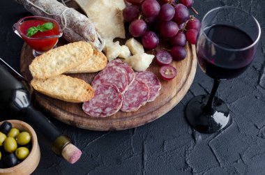 Bir şişe kırmızı şarap şarap kadehi ve antipasti ile. Çeşitli İtalyan tarzı ziyafet Mama seti. Lezzetli Aperatif partisi. Salam, ekmek, sos, üzüm ve Parmesan peyniri ile yönetim kurulu. Kopya alanı.