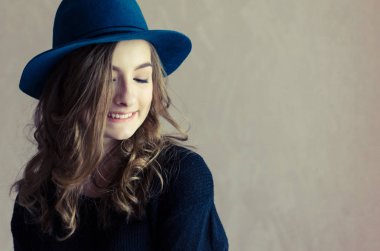 Mavi şapka ve siyah jumper aşağı bakıyor uzun adil kıvırcık saçlı güzel gülümseyen hipster genç kız portresi. Yaşam tarzı ve insanlar kavramı. Tonlu görüntü. Kopya alanı.