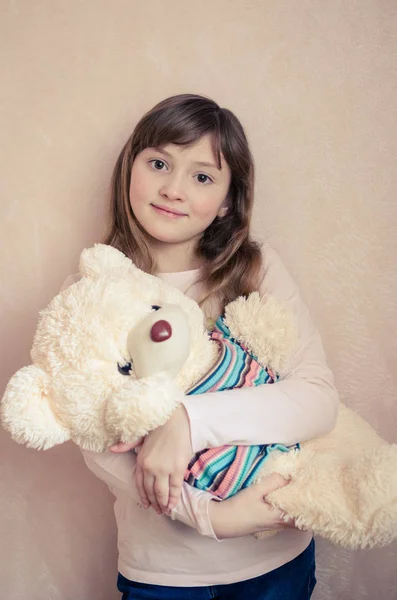 Little girl 8 years old with a big teddy bear on pink background smiling and loves toys stuffed animals. A beautiful child with wonderful expressive brown eyes and a charming smile.