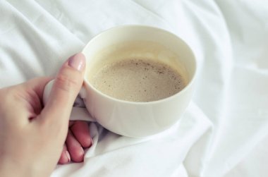 Bir fincan kahve üzerinde beyaz bir battaniye yatakta kadın elinde. Konfor rahat ev atmosfer keyfini Moman. Günaydın. POV.