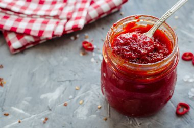 Kırmızı sıcak biber reçeli cam gri beton zemin üzerine taze malzemelerle. Doğal ev yapımı biber sosu kaşıkla. Taze ev yapımı salsa sosu. Kopya alanı.