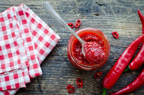 Kırmızı sıcak biber reçeli cam eski ahşap zemin üzerine taze malzemelerle. Doğal ev yapımı biber sosu kaşıkla. Taze ev yapımı salsa sosu. Üstten görünüm.