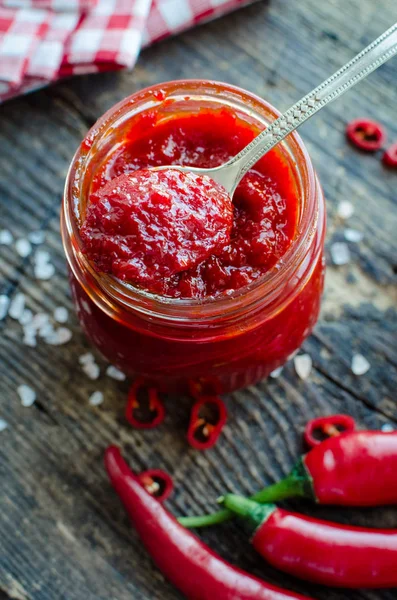 Kırmızı sıcak biber reçeli cam eski ahşap zemin üzerine taze malzemelerle. Doğal ev yapımı biber sosu kaşıkla. Taze ev yapımı salsa sos.