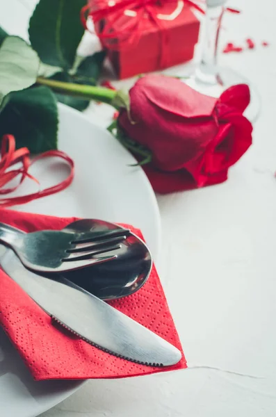 Close up view of restaurant table with romantic place setting with red roses, plates, cutlery on white background. Valentine\'s Day or romantic dinner concept. Valentine day or proposal background.