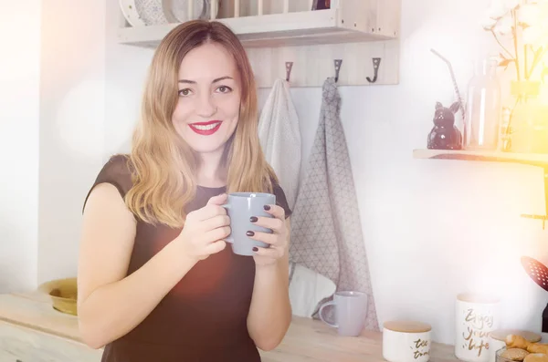 Portrait of smiling young woman with cup against kitchen interior background.