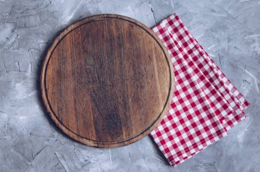 Boş yuvarlak ahşap kesme tahtası üzerinde kırmızı kareli peçete oconcrete arka plan metin için yer ile. Mutfak arka plan yemek. Üstten görünüm. Kopya alanı.