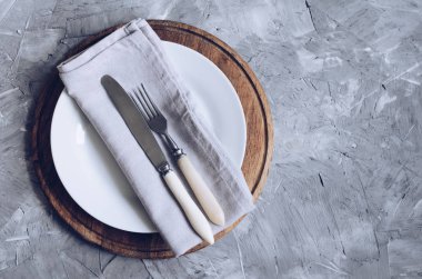 Çatal, bıçak, gri kumaş peçete ve metin için yer beton zemin üzerine ahşap tahta üzerinde beyaz tabak. Gıda arka plan. Güzel anlaşma. Menü mockup. Düz yatıyordu. Üstten görünüm. Kopya alanı.