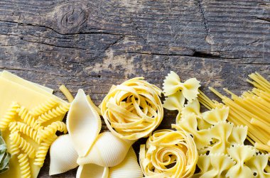 Çeşitli türleri ve İtalyan makarna yukarıdan eski ahşap arka plan üzerine şekiller. İtalyan mutfağı gıda kavramı ve menü tasarımı. Kuru makarna arka plan. Üstten görünüm. Düz yatıyordu. Kopya alanı.